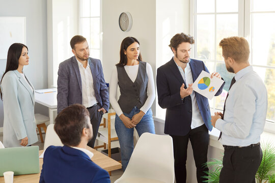 Confident business team analyzing pie chart during presentation in bright office. Male speaker explaining financial data to attentive colleagues, discussing strategies and plans for company growth.