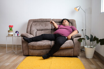 Obraz premium Fat Man Relaxing on Sofa with Remote Control Enjoying Relaxing Time in the Comfort of Home