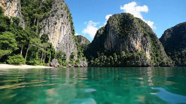 Tropical seascape featuring towering jungle covered limestone karsts rising from turquoise ocean water near a secluded beach