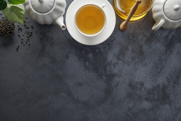 Fresh tea in a white ceramic cup, honey, honey spoon, teapot, tea leaves on the table. Top viev