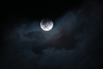 Full moon shining through soft clouds in the blue night sky