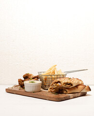 Cheesy chicken rolls with French fries, fried chicken wings, and dipping sauce on wooden board