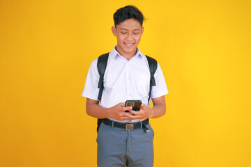 Cheerful Young Student Smiling While Texting on Mobile Phone Against Vibrant Yellow Backdrop