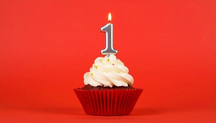 Cupcake with white frosting and lit number one candle in red liner on red background.
