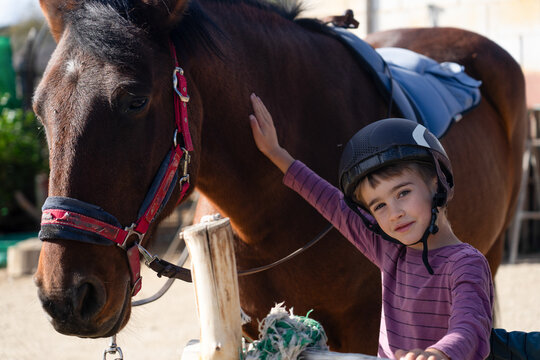 Young child petting horse wearing riding helmet, equestrian experience
