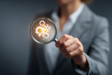 a businesswoman in a suit holds a magnifying glass with a light bulb and gears icon over her hand on a blurred office background, representing the concept of business ideas and innovative technology.
