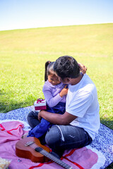 Fototapeta premium Father Tenderly Hugs his Daughter While She Looks at the Gift She Gave Him During Picnic