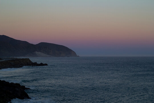 Coastal cliffs and ocean at dusk under colorful twilight sky