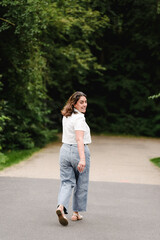 Obraz premium Woman looks back playfully while walking toward a shaded forest path.