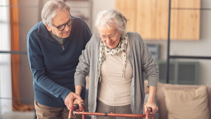 An elderly couple helps each other while using a walking frame