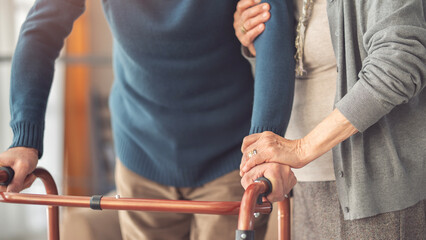An elderly couple helps each other while using a walking frame