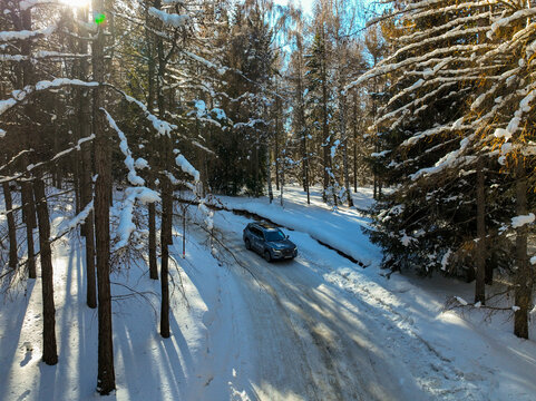 Karakol, Kyrgyzstan - December 13, 2024: Directly overhead view of a gray MG RX8 SUV with DRLs on driving on a partially cleared snow covered road surrounded by dark, winter forest foliage