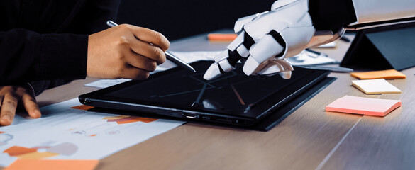 A human and a robot engage in a collaborative design process, using a touchscreen tablet to merge technology with creativity in a modern workspace.Noogenesis