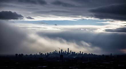 City skyline silhouette during a dramatic winter storm with sun rays illuminating through dark clouds. Urban winter weather concept.