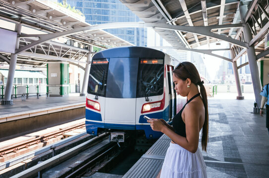Woman looking at smartphone at BTS skytrain station, Bangkok, Thailand