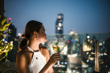 Young asian woman drinking a cocktail on a rooftop bar, Bangkok, Thailand