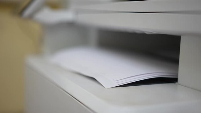 Many of A4 white paper were printing out from photocopy machine in fast motion, Close-up with selective focus.