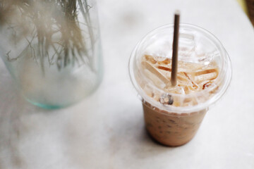 A plastic glass of ice latte coffee with milk foam and pink orchid flower decorated on wooden table