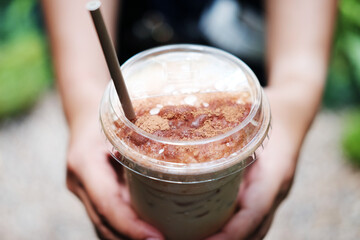 Close up hand holding a plastic glass of ice latte coffee with chocolate powder on topping 