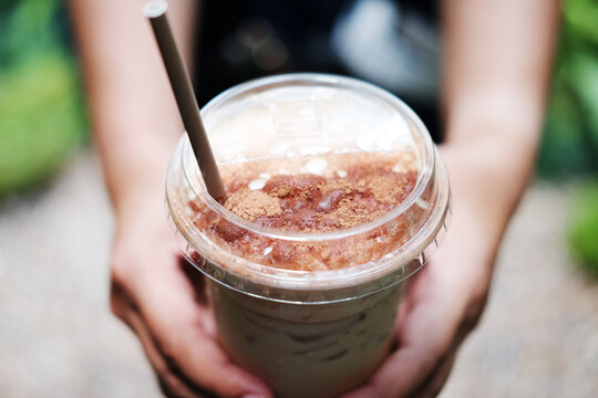 Close up hand holding a plastic glass of ice latte coffee with chocolate powder on topping - Powered by Adobe
