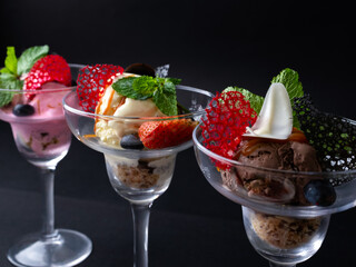 Three Gourmet Ice Cream Parfaits with Strawberries, Caramel, and Chocolate Served in Elegant Glasses on a Dark Background