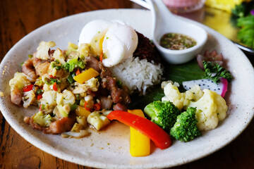 Close up stir-fried pork with cauliflower with boiled egg, fish sauce, broccoli and raspberry rice on a white plate
