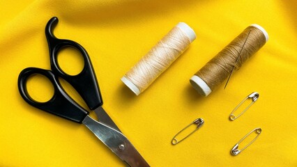 Scissors, thread, and pins on yellow fabric. Concept: professional tailoring, handcrafted work, quality, and attention to detail.