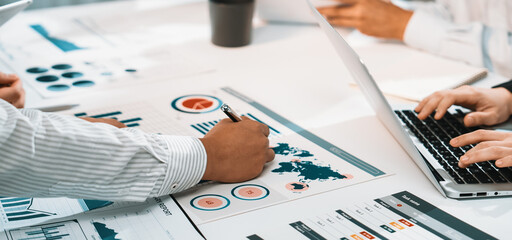 A diverse team engages in a dynamic meeting focused on business analytics. They analyze reports, charts, and graphs while collaborating in a modern office environment. SACTR