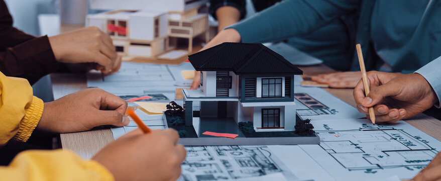A dynamic group engaged in architectural planning, featuring hands working on blueprints with a model house at the center, showcasing teamwork and creativity in design. SACTR
