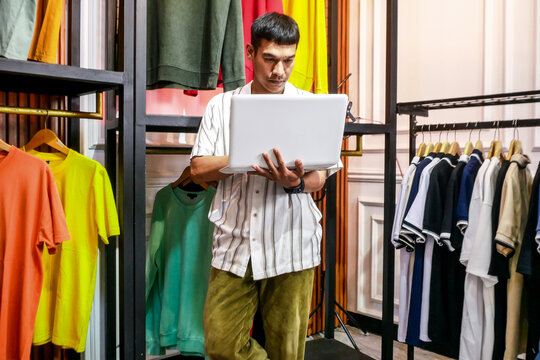 Asian Entrepreneur Managing Inventory With Laptop in Trendy Clothing Store