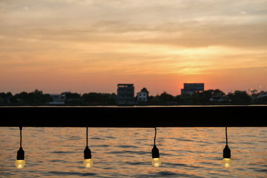 Close up of light bulb, hanging string light with bokeh sunset view along the river