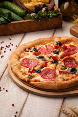 Hot pepperoni pizza topped with olives, tomatoes, mushrooms and melted cheese on a wooden board