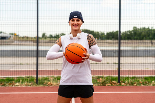 Portrait of young female street basketball athlete holding ball and smiling.