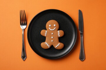 Gingerbread man on a black plate with silverware set against an orange background