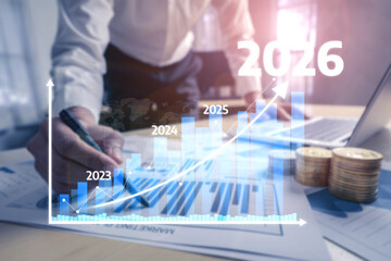 A businessman reviews charts and financial projections for 2023 to 2026, highlighting growth and trends in a modern office environment with documents and technology. Tessel
