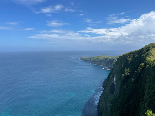 A breathtaking view from a high cliff overlooking a tropical coastline with turquoise and deep blue ocean waters.