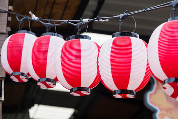 Row of traditional red and white Japanese paper lanterns hanging outdoors under a roof structure during a cultural celebration