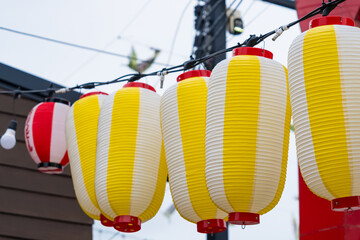 Row of yellow and white Japanese paper lanterns hanging outdoors in a festive urban street setting