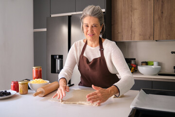 Senior woman in apron preparing pizza dough on a kitchen counter
