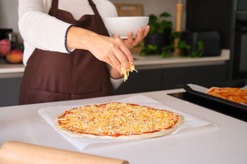 Hands sprinkling shredded cheese topping on an uncooked pizza for baking