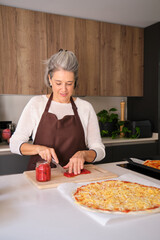 Senior woman cutting vegetables for a delicious homemade pizza in a modern kitchen