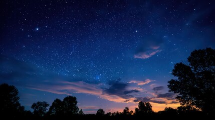 Naklejka premium Starry Night Sky with Dark Silhouetted Trees and Hues of Blue Orange and Purple at Dusk with Scattered Clouds and Stars Twinkling Above Scenic Landscape