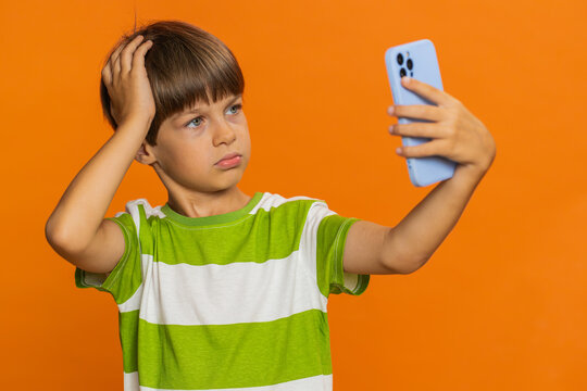 Upset sad preteen child boy kid use smartphone typing browsing, play game, loses, surprised by sudden lottery results, bad fortune, loss, fail, unlucky news. Sad children on orange background indoors