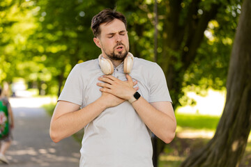 Young adult sports man runner jogger having heart attack or chest pain after running workout in urban city park. A tired athlete suffers from tension in the heart. Health care and sports concept.