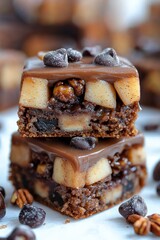 Stacked brownies with apple, caramel, nuts, and chocolate chips on a light surface