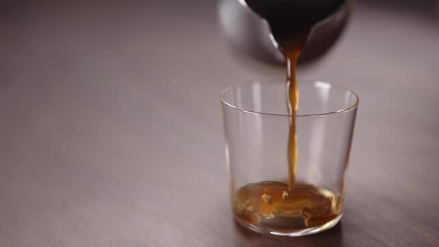Slow motion coffee pour into tumbler glass on walnut table