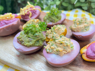 Colorful stuffed eggs and mini bell peppers. The eggs have a pinkish hue and are topped with different fillings, including a green herb mixture, a creamy yellow mixture, and a bright purple spread.
