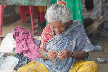 An elderly Indian woman makes jewelry