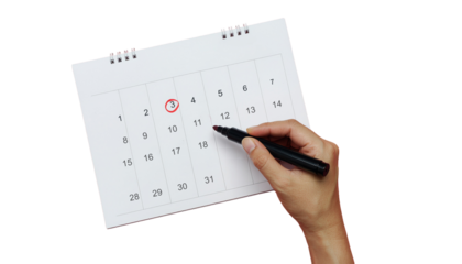 A hand marks date circled in red on calendar isolated on white bg cutout