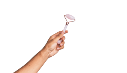 Hand holding a pink facial roller with a metal frame and a cylindrical stone at the end, arm extended. clean white background